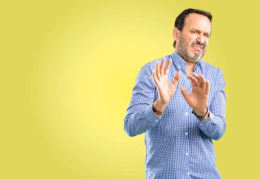 Handsome middle age man disgusted and angry, keeping hands in stop gesture, as a defense, shouting clipart