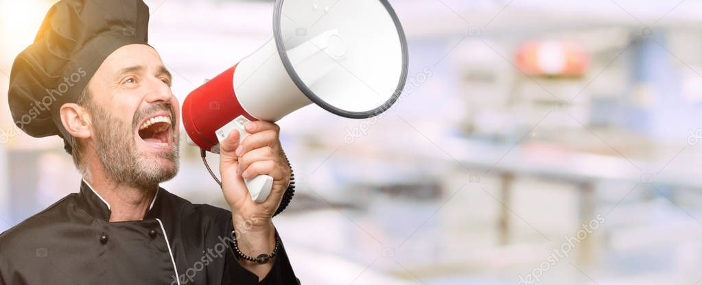 Senior cook man, wearing chef hat communicates shouting loud holding a megaphone, expressing success and positive concept, idea for marketing or sales at restaurant kitchen