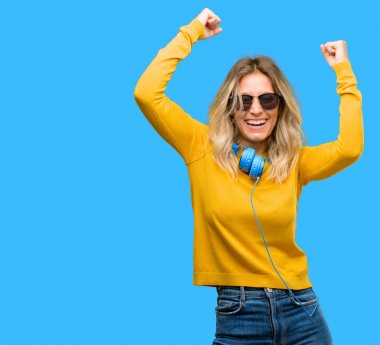 Young beautiful woman with headphones happy and excited celebrating victory expressing big success, power, energy and positive emotions. Celebrates new job joyful clipart