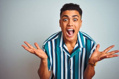 Yazlık çizgili tişört giyen genç Brezilyalı adam izole edilmiş beyaz arka planda durmuş çılgın ve başarıyı kutlarken kolları havada ve gözleri açık heyecanla haykırıyor. Kazanan konsept