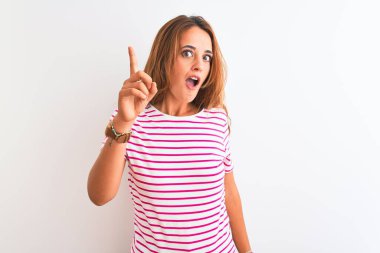 Genç kızıl saçlı kadın, çizgili günlük tişört giyiyor, beyaz izole arka planda parmakla işaret ederek başarılı bir fikir sunuyor. Heyecanlı ve mutlu. Bir numara..