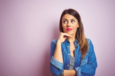 Pembe soyutlanmış arka planda duran genç ve güzel bir kadın. Elleri çenesinde soru sorarken, düşünceli bir ifade takınıyor. Düşünceli bir yüzle gülümsüyor. Şüphe kavramı.