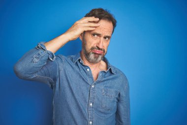 Yakışıklı, orta yaşlı, gri saçlı, soyutlanmış mavi arka planlı, endişeli ve stresli bir adam. Alnındaki sorun yüzünden gergin ve bunalımda.