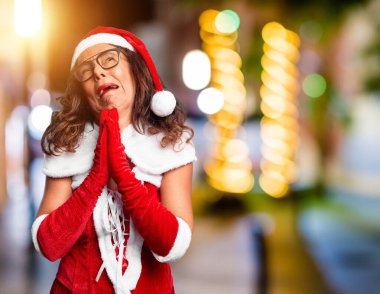Orta yaşlı kadın Noel Baba kostümü giyiyor. Elleriyle yalvarıyor ve dua ediyor. Yüzünde umut ifadesi var. Af diliyor. Din kavramı.