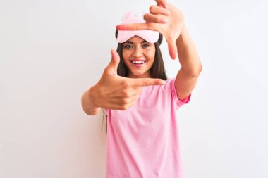 İzole edilmiş beyaz arka planda duran maske takan genç ve güzel bir kadın gülümsüyor ve mutlu yüzlü elleri ve parmakları olan bir çerçeve yapıyor. Yaratıcılık ve fotoğrafçılık kavramı.