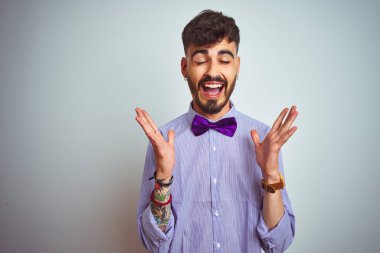 Mor gömlekli ve papyonlu genç adam izole edilmiş beyaz arka planda çılgın ve başarıyı kutluyor kolları havada ve gözleri kapalı heyecanla bağırıyor. Kazanan konsept