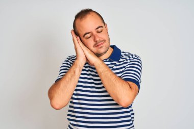 Sıradan çizgili polo giyen genç adam izole edilmiş beyaz arka planda ayakta uyur yorgun düşler kurar ve elleri ile birlikte poz verir ve gözleri kapalı gülümserdi..