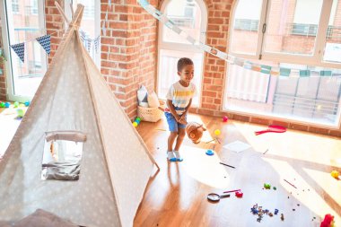Güzel Afrikalı Amerikalı çocuk anaokulunda bir sürü oyuncakla at oyuncağıyla oynuyor.