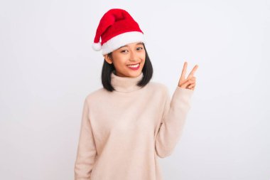 Noel Baba şapkası takan genç, güzel Çinli bir kadın izole edilmiş beyaz arka planda iki numarayı gösterirken kendinden emin ve mutlu bir şekilde gülümsüyor..