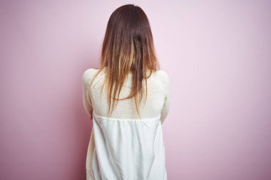 Pembe arka planda duran genç ve güzel bir kadın. Arkaya bakıyor ve kollarını kavuşturuyor.