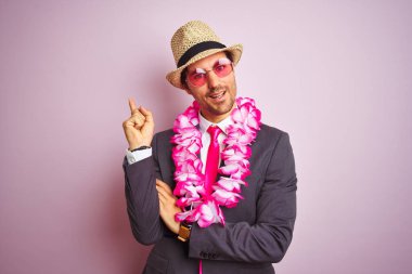 Takım elbiseli genç işadamı gözlüklü Hawai leyleği soyutlanmış pembe arka planda mutlu bir şekilde el ve parmak uçlarını işaret ediyor.
