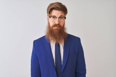 Genç, kızıl saçlı, takım elbiseli ve gözlüklü bir iş adamı izole edilmiş beyaz bir arka plan ve yüzünde ciddi bir ifade var. Basit ve doğal bir şekilde kameraya bakıyorsun..