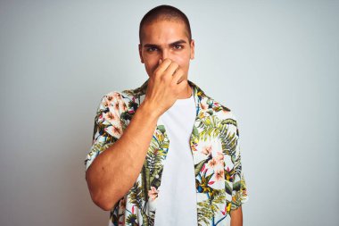 Tatillerde beyaz arka planda Hawaii gömleği giyen genç yakışıklı bir adam pis ve iğrenç bir koku alıyor. Nefesini burnunda tutuyor. Kötü koku konsepti.