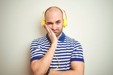 Sarı kulaklık takıp müzik dinleyen genç adam kollarını kavuşturup depresyondan sıkılmış ve yorgun görünüyor..