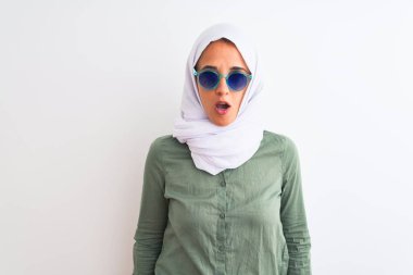 Genç Arap kadın tesettür ve yaz gözlüğü takıyor. İzole bir arkaplanda korku, korku ve heyecan dolu bir yüz ifadesiyle dehşete düşmüş ve şok olmuştu..