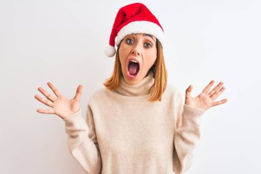 Güzel kızıl saçlı kadın, izole edilmiş arka planda noel şapkası takıyor çılgın ve başarıyı kollarını kaldırıp heyecanla haykırarak kutluyor. Kazanan konsept