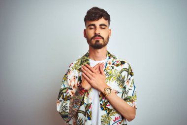 Tatilde dövmeli bir adam izole edilmiş beyaz arka plan üzerinde duruyor elleri göğsünde kapalı ve yüzünde minnet dolu bir jest ile gülümsüyor. Sağlık kavramı.