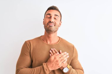 Kışlık süveter giyen yakışıklı, soyutlanmış arka planda gülümseyen, elleri göğsünde, gözleri kapalı ve yüzünde minnet dolu bir jest yapan genç bir adam. Sağlık kavramı.