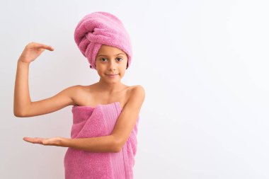 Güzel bir kız çocuğu duş havlusu takıyor. İzole edilmiş beyaz arka plan üzerinde duruyor. Ellerinde büyük ve büyük beden işareti, ölçü sembolü var. Kameraya bakıp gülümsüyor. Ölçüm konsepti.