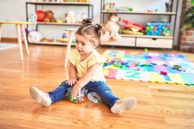 Anaokulunda elinde bir kavanoz çikolata renkli topla yerde oturan güzel çocuk.