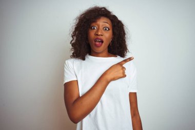 Genç Afro-Amerikalı kadın tişört giyiyor. İzole edilmiş beyaz arka planda duruyor. Parmakla işaret ediyor, ağzı açık hayret içinde..