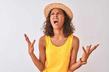 Sarı tişört ve yaz şapkası giyen genç Brezilyalı kadın izole edilmiş beyaz arka planda çılgınca bağırıyor ve agresif bir ifade ve kollarla bağırıyor. Hayal kırıklığı konsepti.