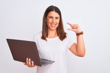 Güzel genç bir kadın bilgisayarla beyaz arka plan üzerinde çalışıyor gülümsüyor ve kendinden emin bir şekilde el hareketi yapıyor parmaklarıyla işaret yapıyor ve kameraya bakıyor. Ölçü kavramı.