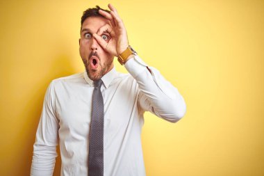 Sarı izole edilmiş arka plan üzerinde zarif beyaz gömlek giyen genç yakışıklı iş adamı şaşırmış yüz ve parmaklarından bakan gözlerle iyi bir jest yapıyor. İnançsız ifade.