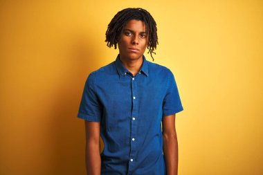 Rastgele kot gömlekli Afro adam izole edilmiş sarı arka planda duruyor. Yüzünde ciddi bir ifadeyle rahatlamış. Basit ve doğal bir şekilde kameraya bakıyorsun..