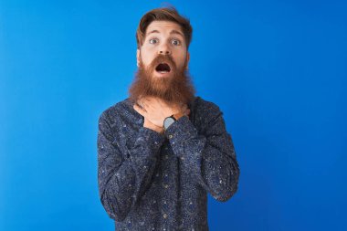 Çiçekli yaz gömleği giyen genç kızıl saçlı adam izole edilmiş mavi arka planda durup bağırıyor ve boğuluyor çünkü acı verici bir boğulma. Sağlık problemi. Boğulma ve intihar konsepti.