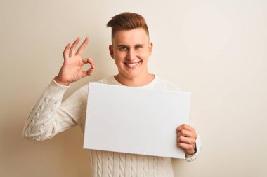 İzole edilmiş beyaz arka planda afiş tutan genç yakışıklı adam tamam işareti yapıyor, mükemmel bir sembol.