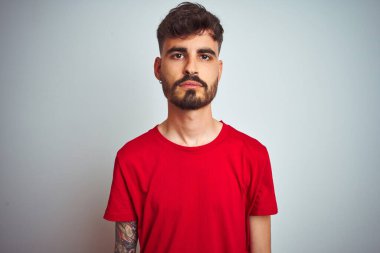 İzole edilmiş beyaz arka planda duran kırmızı tişörtlü genç adam yüzünde ciddi bir ifadeyle rahatlamış. Basit ve doğal bir şekilde kameraya bakıyorsun..