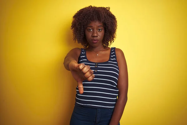 孤立した黄色の背景に縞模様のTシャツを着た若いアフリカのアフロ女性は 親指ダウンジェスチャーで不満と怒りの拒絶と否定を示しています 悪い表現 — ストック写真