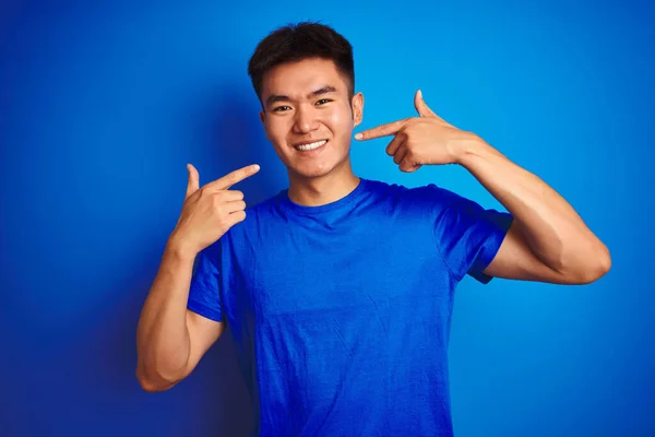 Tシャツを着た若いアジア系中国人男性は 指の歯と口で陽気に見せ 指差す青い背景の上に立っています 歯科衛生の概念 — ストック写真