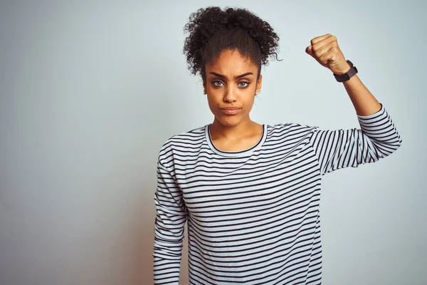 African american woman wearing navy striped t-shirt standing over isolated white background Strong person showing arm muscle, confident and proud of power