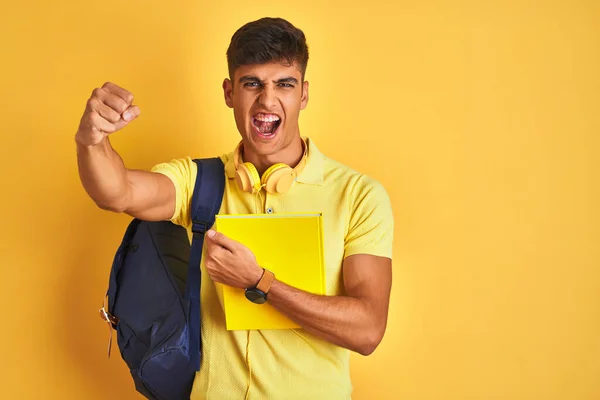 孤立した黄色の背景にバックパックのヘッドフォンノートブックを身に着けているインドの学生の男がいらいらし 怒りで叫んで 狂気と大声で手を上げ 怒りの概念 — ストック写真