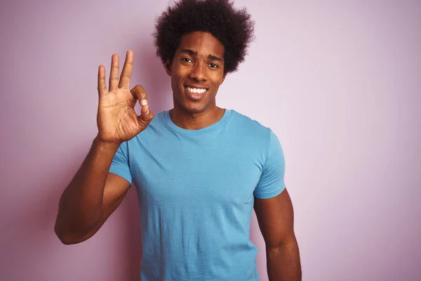 黑头发的非裔美国人穿着蓝色T恤 站在孤立的粉色背景上 微笑着 手指手画脚地签了名 成功表达 — 图库照片