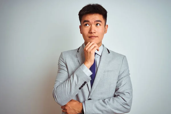 グレーのジャケットを着たアジア系中国人の実業家は 顎の質問について考えて手で隔離された白い背景の上に立ってネクタイ 集中的な表現 思慮深い顔で微笑んだ 疑いの概念 — ストック写真