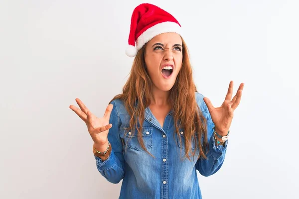 孤立した背景にクリスマスの帽子を身に着けている若い美しい赤毛の女性は狂気と怒鳴り声を上げ 積極的な表現と腕を上げて叫びました 欲求不満の概念 — ストック写真