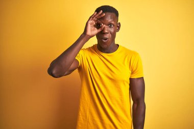Sıradan tişörtler giyen genç Afro-Amerikan bir adam izole edilmiş sarı arka planda dikiliyor. Şaşırmış bir yüz, parmaklarından bakan bir gözle şaşırmış bir hareket yapıyor. İnançsız ifade.