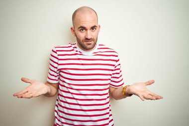 Sakallı, beyaz izole edilmiş arka plan üzerine sıradan kırmızı tişörtlü genç kel bir adam. Hiçbir şeyden habersiz ve kolları açık, hiçbir fikri yok..
