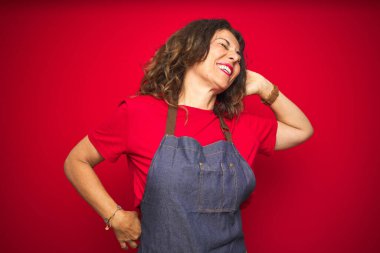 Kırmızı izole arka planda önlük giyen orta yaşlı bir kadın yorgun ve rahat, uykulu ve sabahın erken saatlerinde esniyor.