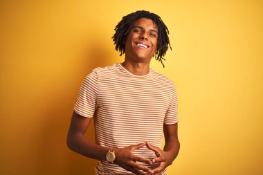 Sarı arka plan üzerinde duran çizgili tişörtlü Afro bir adam ellerini birleştirip gülümseyerek gevşemiş ve neşeli olmasını diliyordu. Başarı ve iyimser