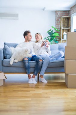 Karton kutular etrafında yeni evde kahve içme kanepede oturan köpek ile genç güzel çift