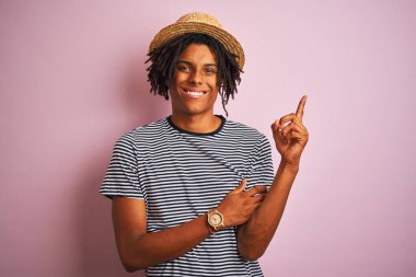 Siyah tişörtlü ve şapkalı Afro-Amerikan bir adam izole edilmiş pembe arka planda, yüzünde kocaman bir gülümsemeyle kameraya el ve parmak şeklinde bakıyor..