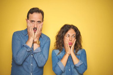 Güzel bir orta yaşlı çift, izole edilmiş sarı arka planda dikiliyorlar. Yüzü, depresyonu ve üzüntüyü örten yorgun eller, sorun yüzünden üzgün ve sinirli.
