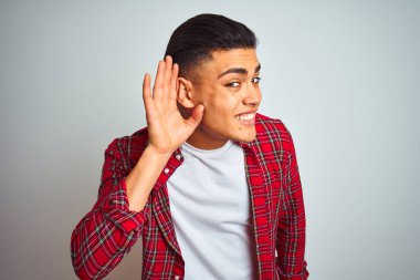 İzole edilmiş beyaz arka planda dikilen kırmızı tişörtlü genç Brezilyalı bir adam kulağına fısıldayarak dedikoduları ve dedikoduları dinliyor. Sağırlık kavramı.