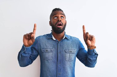 Örgülü, beyaz arka planda kot gömlek giyen Afro-Amerikan bir adam şaşırmış ve şaşırmış bir şekilde yukarı bakıp parmaklarını göstermiş ve kollarını kaldırmıştı..