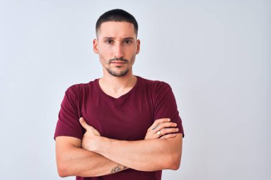 Soyutlanmış arka planda duran genç yakışıklı adam şüpheci ve gergin, yüzünde çapraz kollu tasvip etmeyen ifade. Negatif kişi.