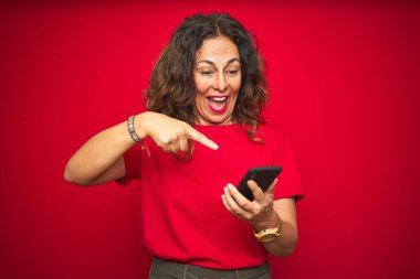 Orta yaşlı bir kadın kırmızı arka plan üzerinde akıllı telefon kullanıyor. El ve parmak ile işaret ederek çok mutlu.